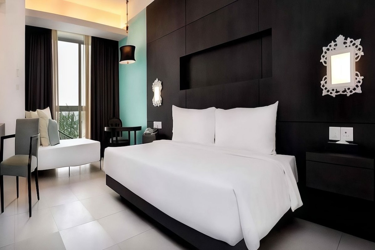 A modern hotel room with a large bed, a desk, and a chair.