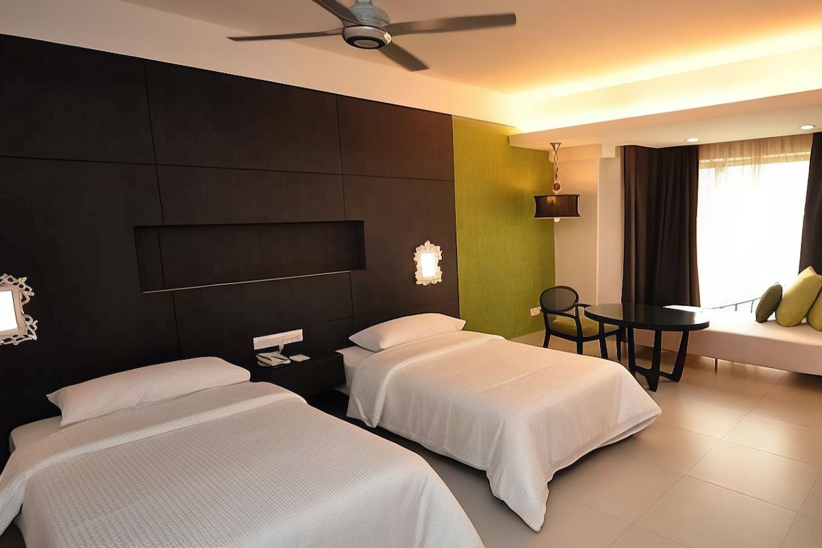 A hotel room with two beds, a ceiling fan, a small table with chairs, and a sofa with cushions.
