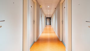 Un largo y estrecho pasillo de hotel con puertas a ambos lados y suelo alfombrado.