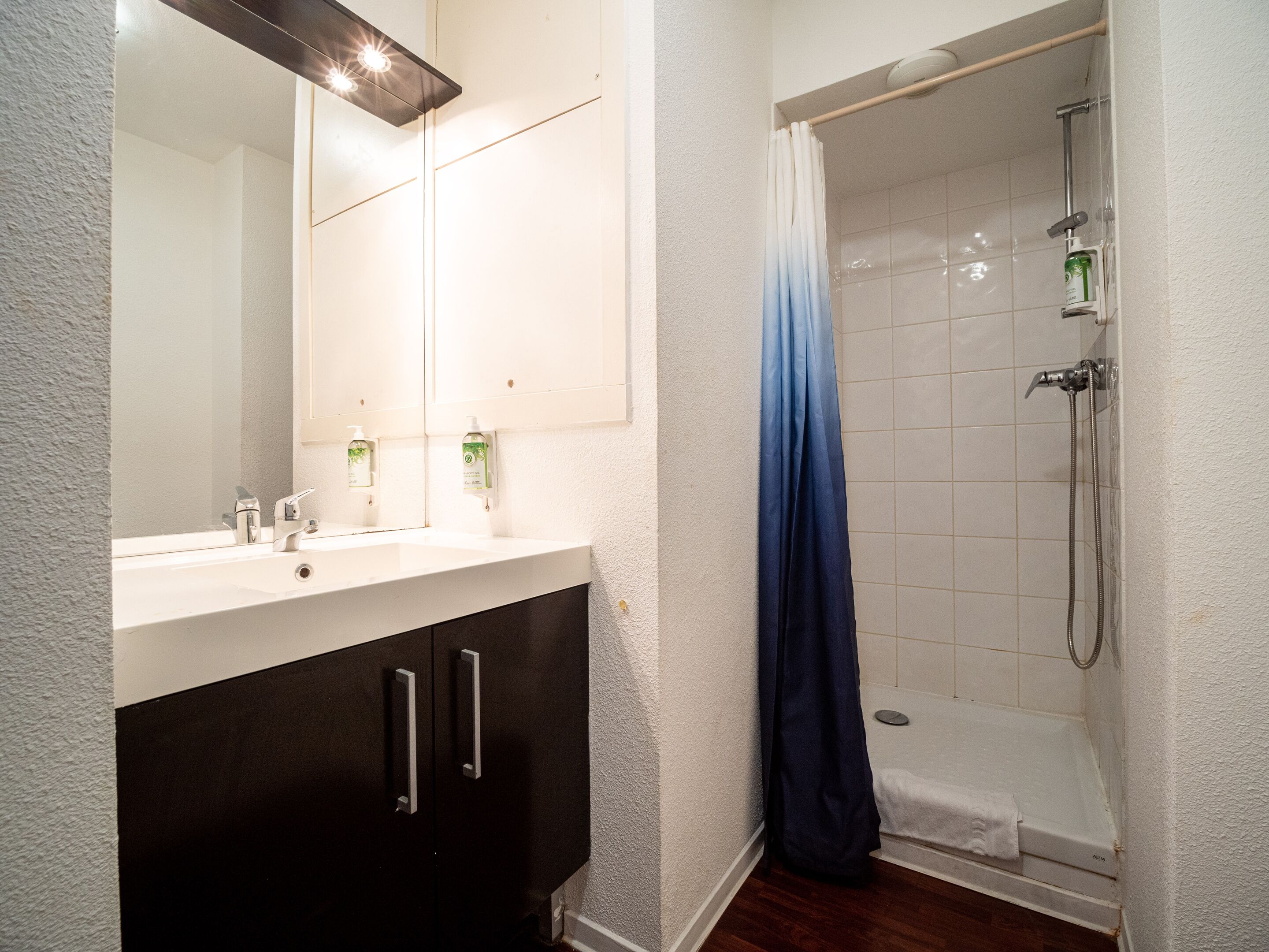Un baño con un lavabo blanco, armarios oscuros, una ducha con cortina azul y un espejo sobre el lavabo.