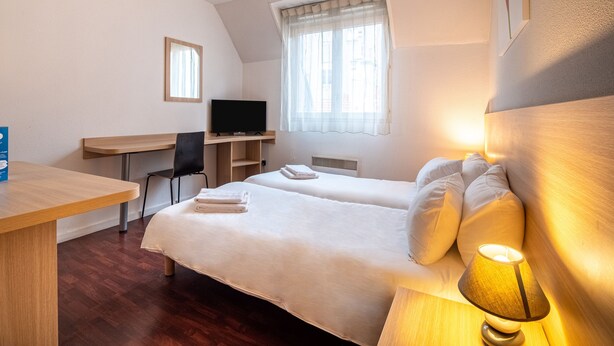 Habitación de hotel con dos camas, un escritorio, una silla, un televisor y una ventana con cortinas.