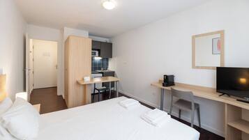 A hotel room with a bed, a desk with a TV, a kitchenette, and a bathroom.