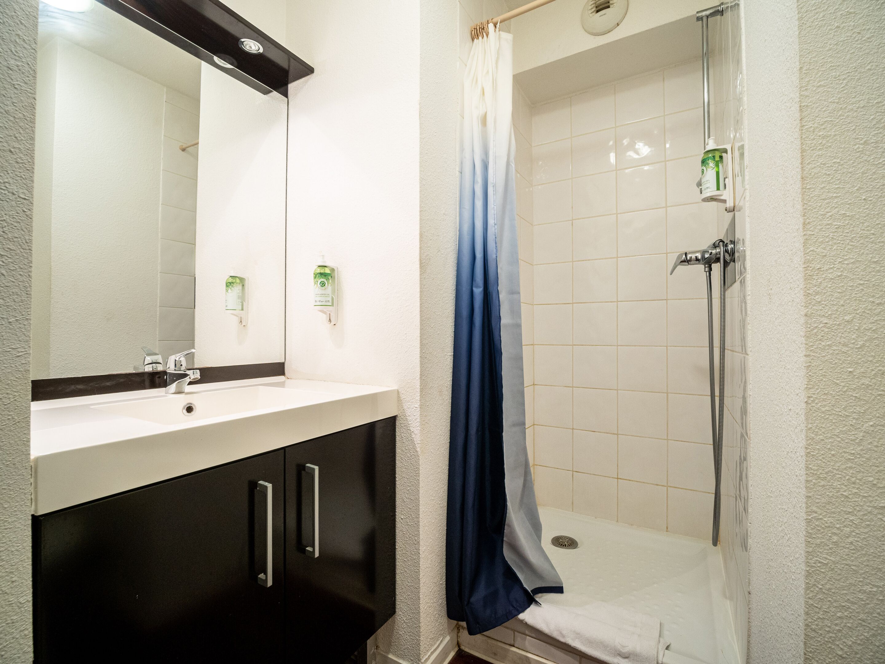 Une salle de bain avec un lavabo blanc, un meuble noir et une douche avec un rideau bleu.
