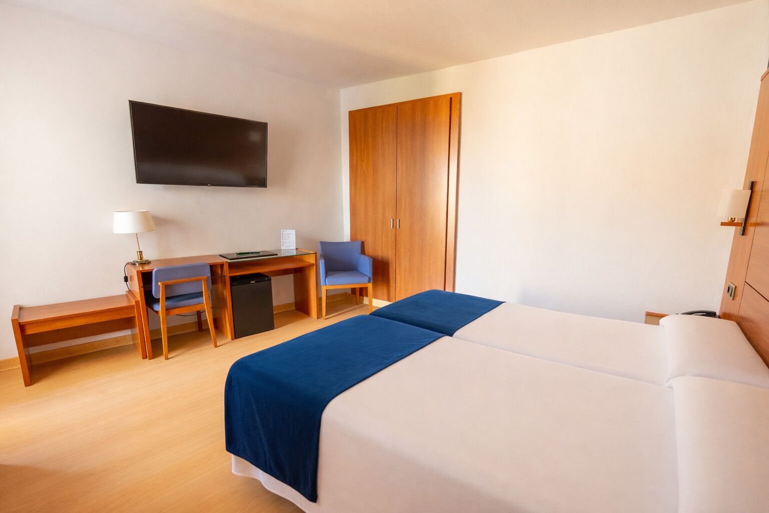 Ein Hotelzimmer mit Bett, Schreibtisch, Sessel, Fernseher und Kleiderschrank.