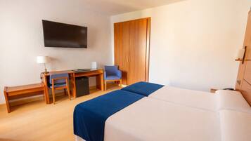 Ein Hotelzimmer mit Bett, Schreibtisch, Sessel, Fernseher und Kleiderschrank.