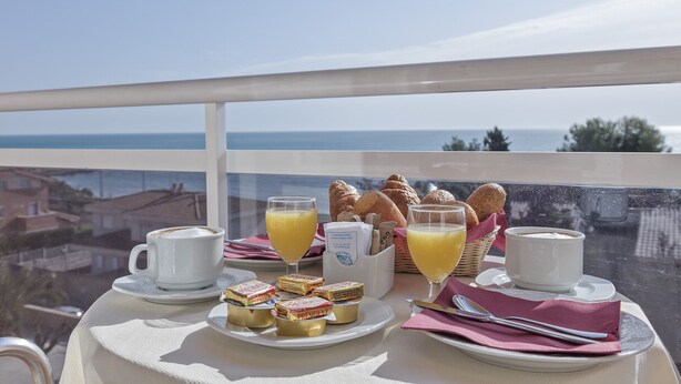 A table with breakfast items including croissants, juice, and pastries, with a view of the sea. - Hotel Sant Jordi (Tarragona)