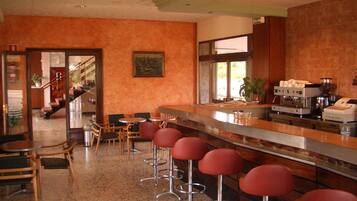 Una zona de bar con taburetes rojos, una cafetera y una escalera que sube a otro nivel.