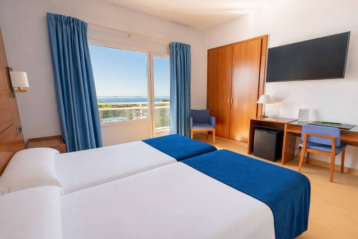 A hotel room with a bed, desk, chair, and a TV.