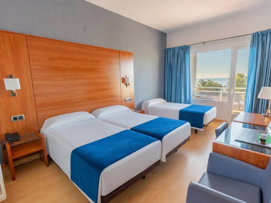 Habitación de hotel con dos camas, un escritorio, una silla, un radiador y una ventana con cortinas.
