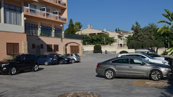 Ein Parkplatz mit mehreren Autos, ein Mehrfamilienhaus mit Balkonen und ein gepflegter Gartenbereich.