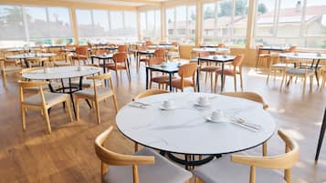A spacious dining area with round tables and chairs, large windows, and a view of the outside.