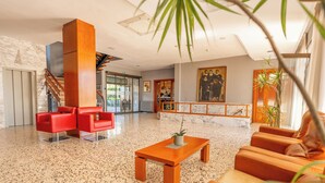 A spacious lobby with a marble floor, red and orange seating, a staircase, and a large painting on the wall. - Hotel Sant Jordi (Tarragona)