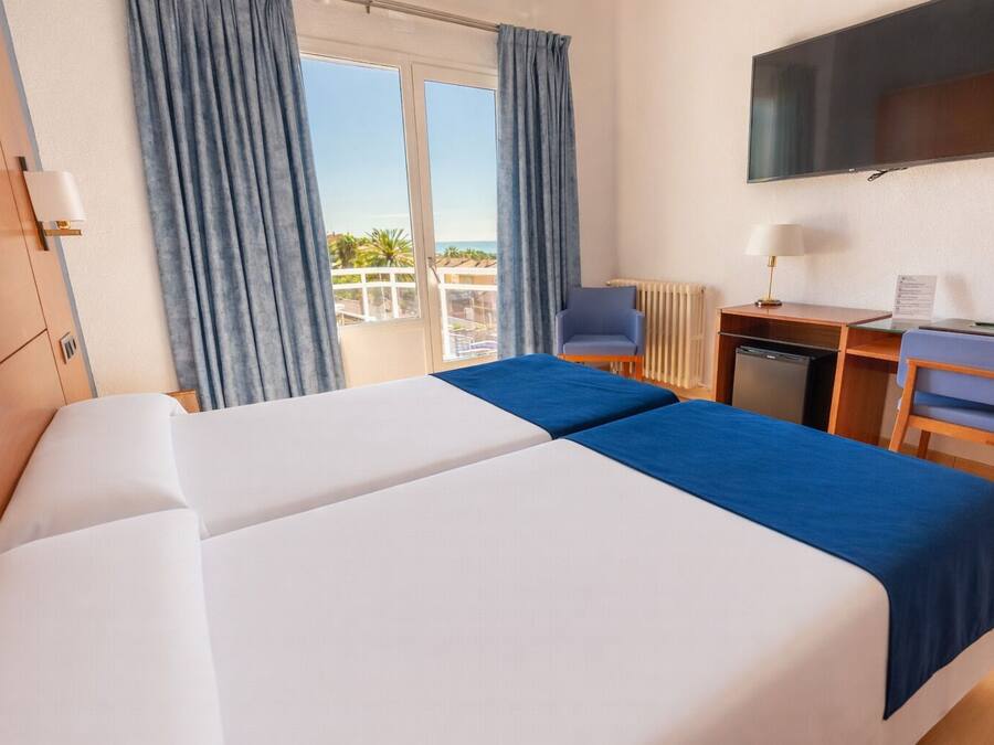 Une chambre d’hôtel avec deux lits, un bureau, une chaise, une télévision et une vue sur la mer.