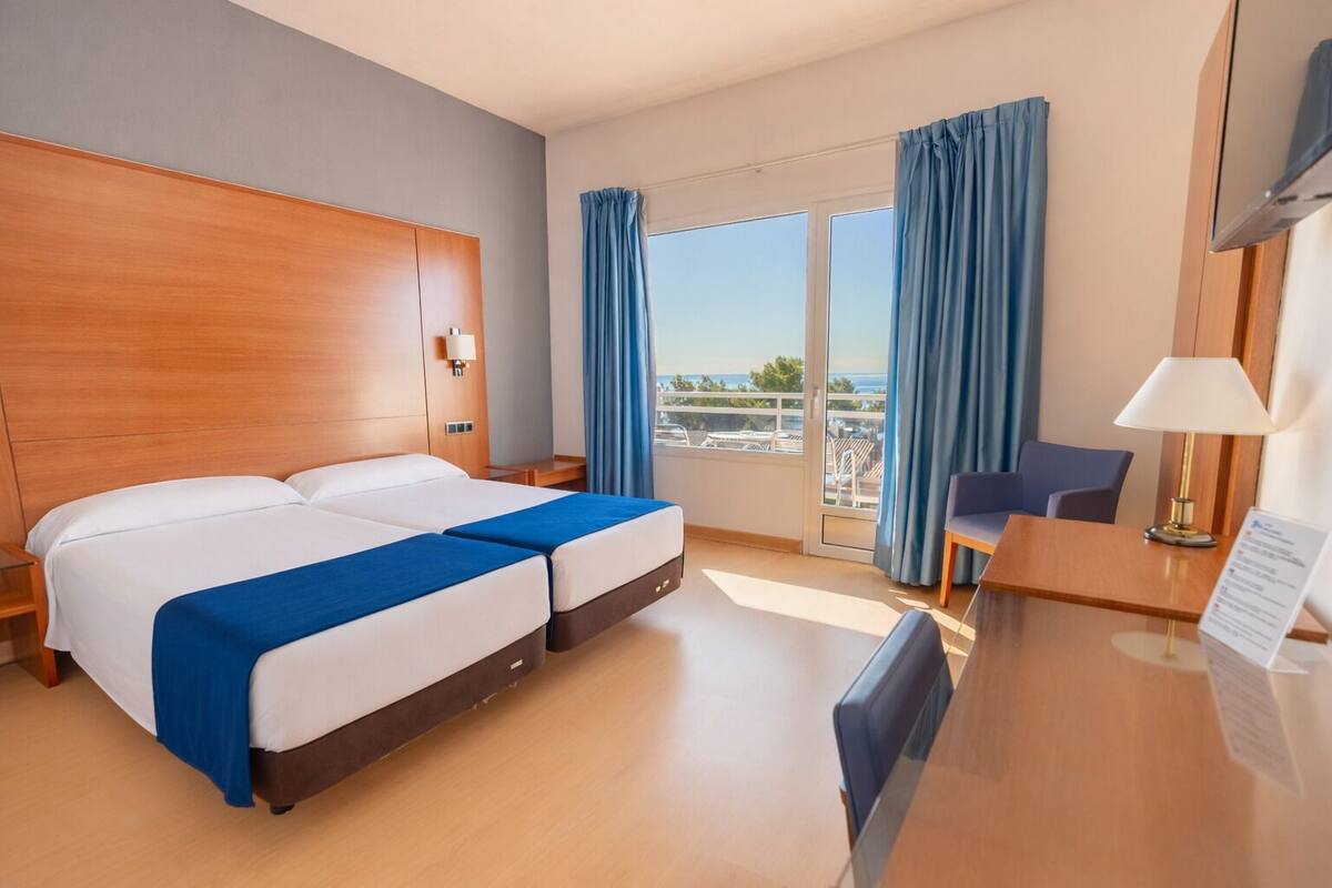 A hotel room with a large bed, a desk, and a view of the sea.