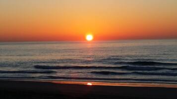 A sunset over the ocean with waves approaching the shore.