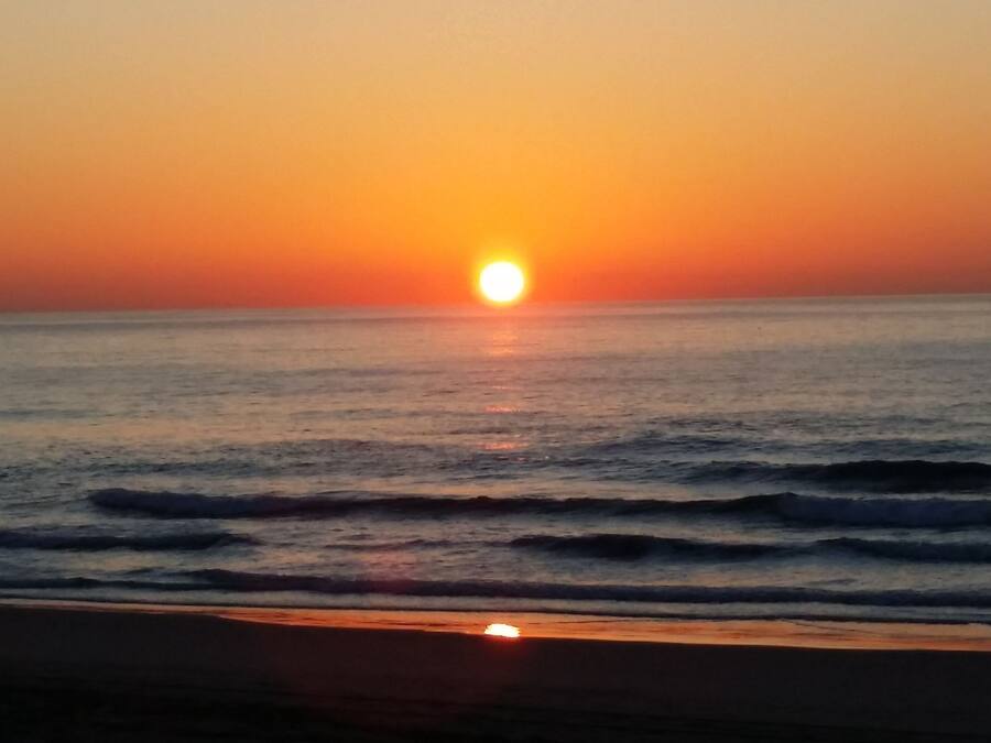 A sunset over the ocean with waves approaching the shore.