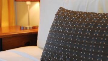 Un lit bien fait, avec du linge de lit blanc et un coussin à motifs, une table de chevet en bois avec une lampe, et une tête de lit en métal.