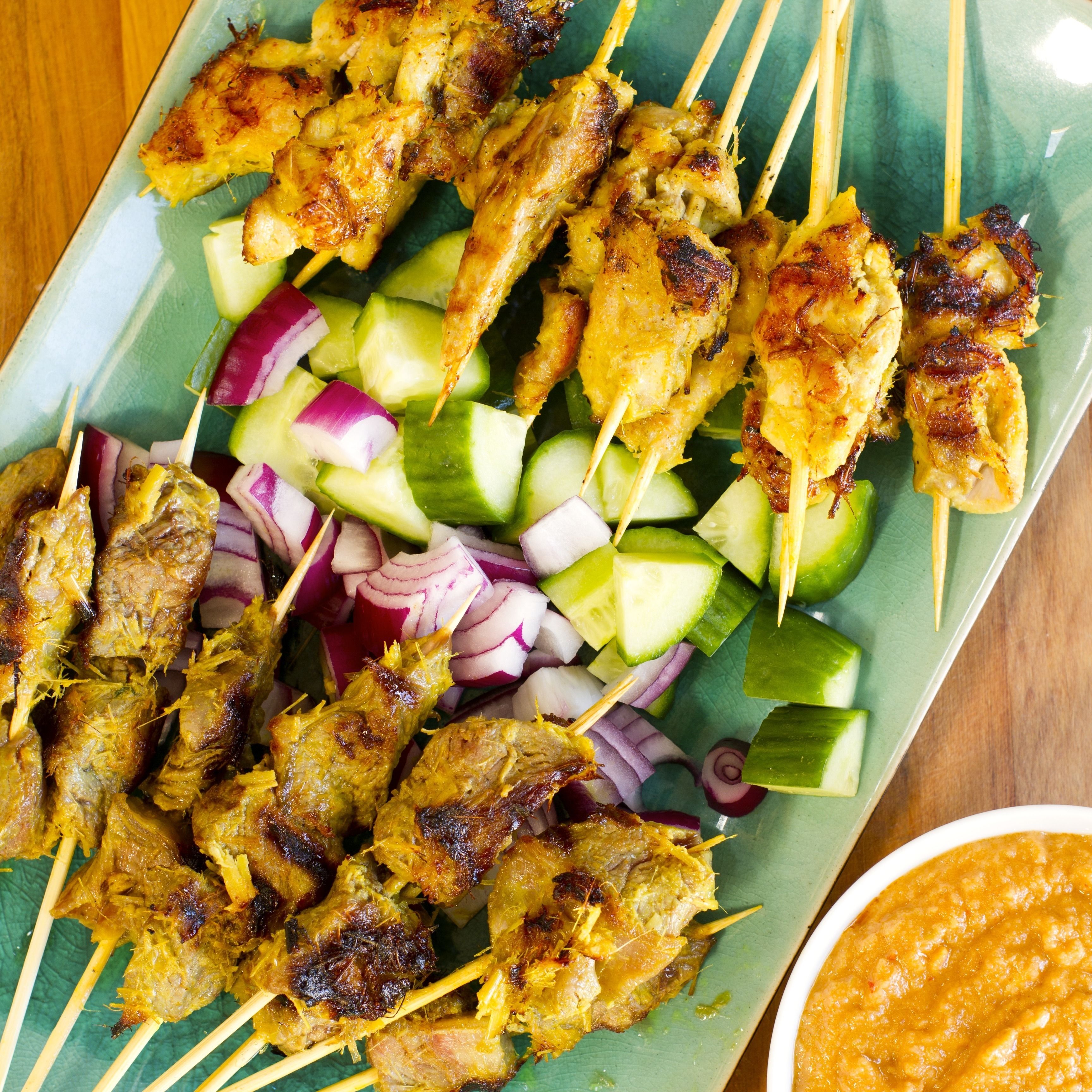 A plate of grilled chicken skewers with cucumber and red onion slices.