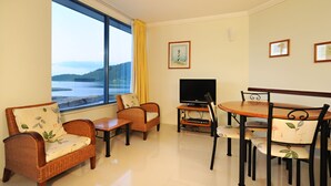 A living room with wicker furniture, a flat-screen TV, and a view of the sea. - at Whitsunday Vista Holiday Apartments (Airlie Beach)
