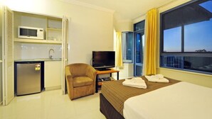 A hotel room with a bed, a TV, a small kitchenette, and a chair. - at Whitsunday Vista Holiday Apartments (Airlie Beach)