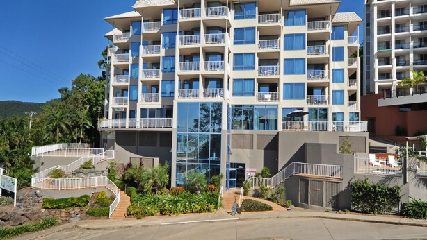 A multi-story hotel with balconies, a central glass facade, and a landscaped entrance area. - at Whitsunday Vista Holiday Apartments (Airlie Beach)