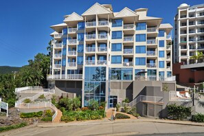 A multi-story hotel with balconies, a central glass facade, and a landscaped entrance area. - at Whitsunday Vista Holiday Apartments (Airlie Beach)