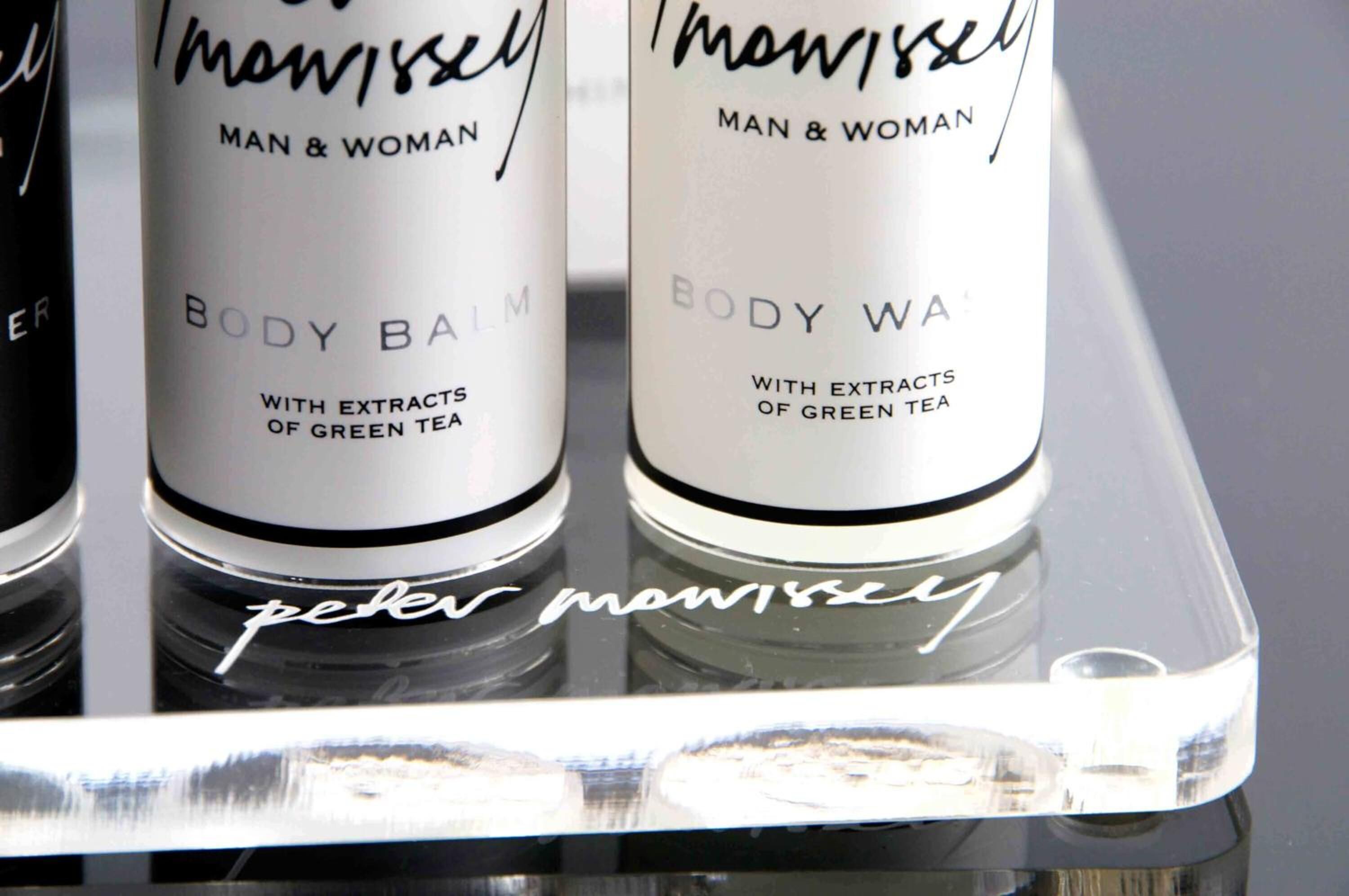 Three bottles of 'Peter Mawissel' body balm on a reflective surface.