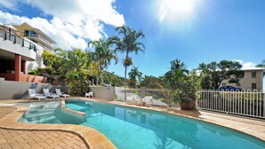 A swimming pool with lounge chairs, palm trees, and a clear sky. - at Whitsunday Vista Holiday Apartments (Airlie Beach)