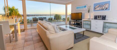A modern living room with a sofa, coffee table, and TV, overlooking a scenic waterfront view.