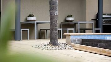 A modern indoor space with a central tree, a stone bench, and two potted plants on tables.
