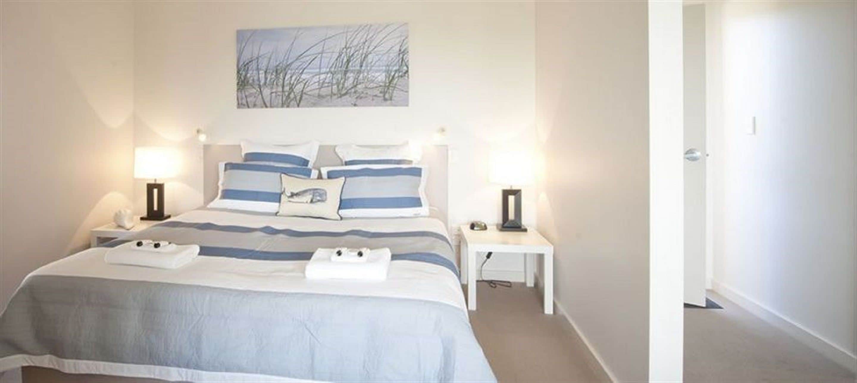 A neatly made bed with a striped bedspread, two bedside tables with lamps, and a painting above the bed.