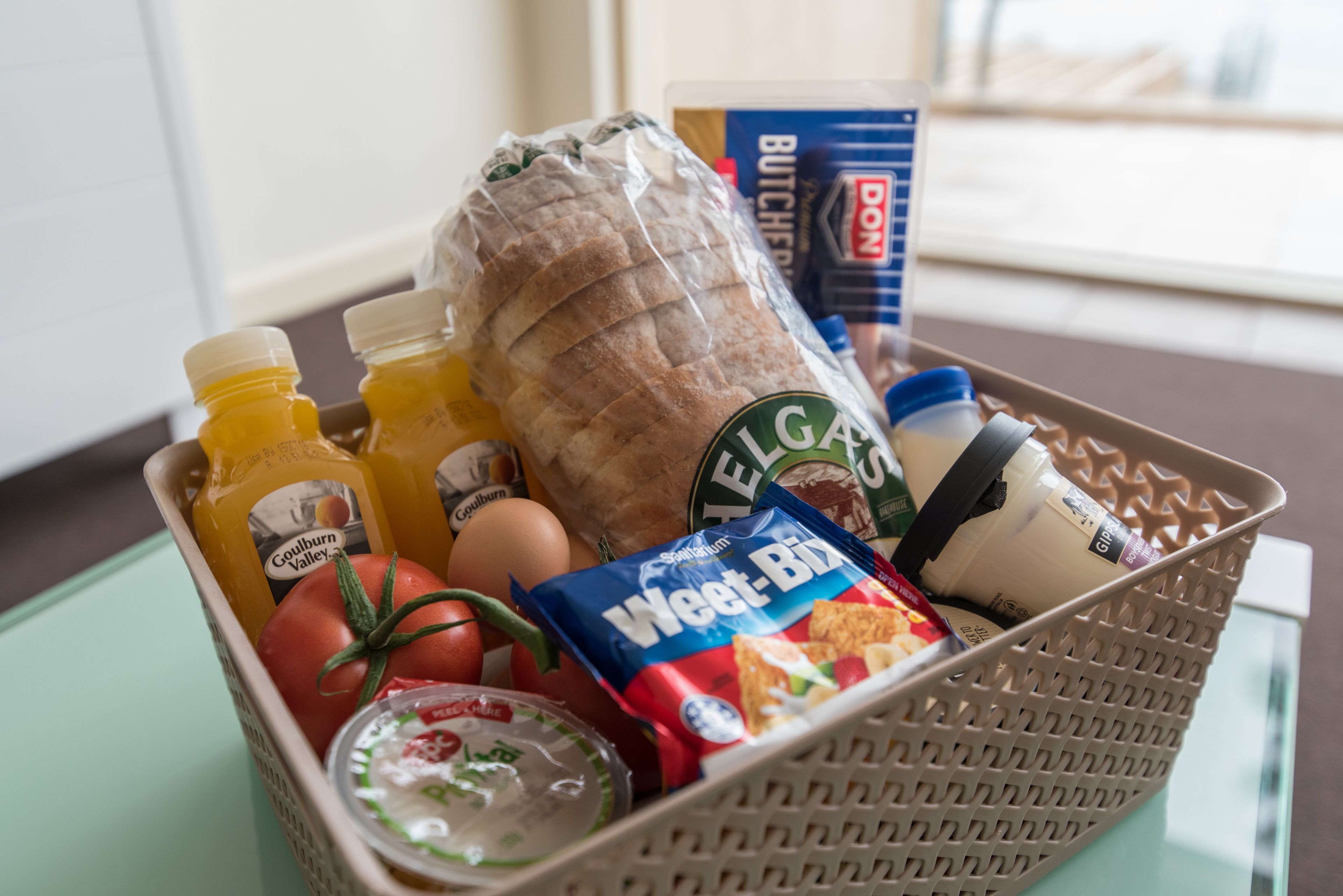 A basket containing bread, eggs, tomatoes, a bottle of juice, a bag of chips, and a container of yogurt.