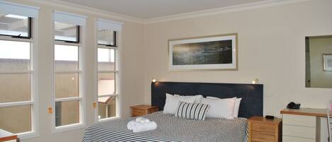 A neatly arranged bedroom with a large bed, a bedside table, a desk, and a chair.
