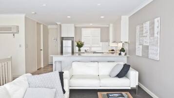 A modern living room with a white sofa, a coffee table, and a kitchen in the background.