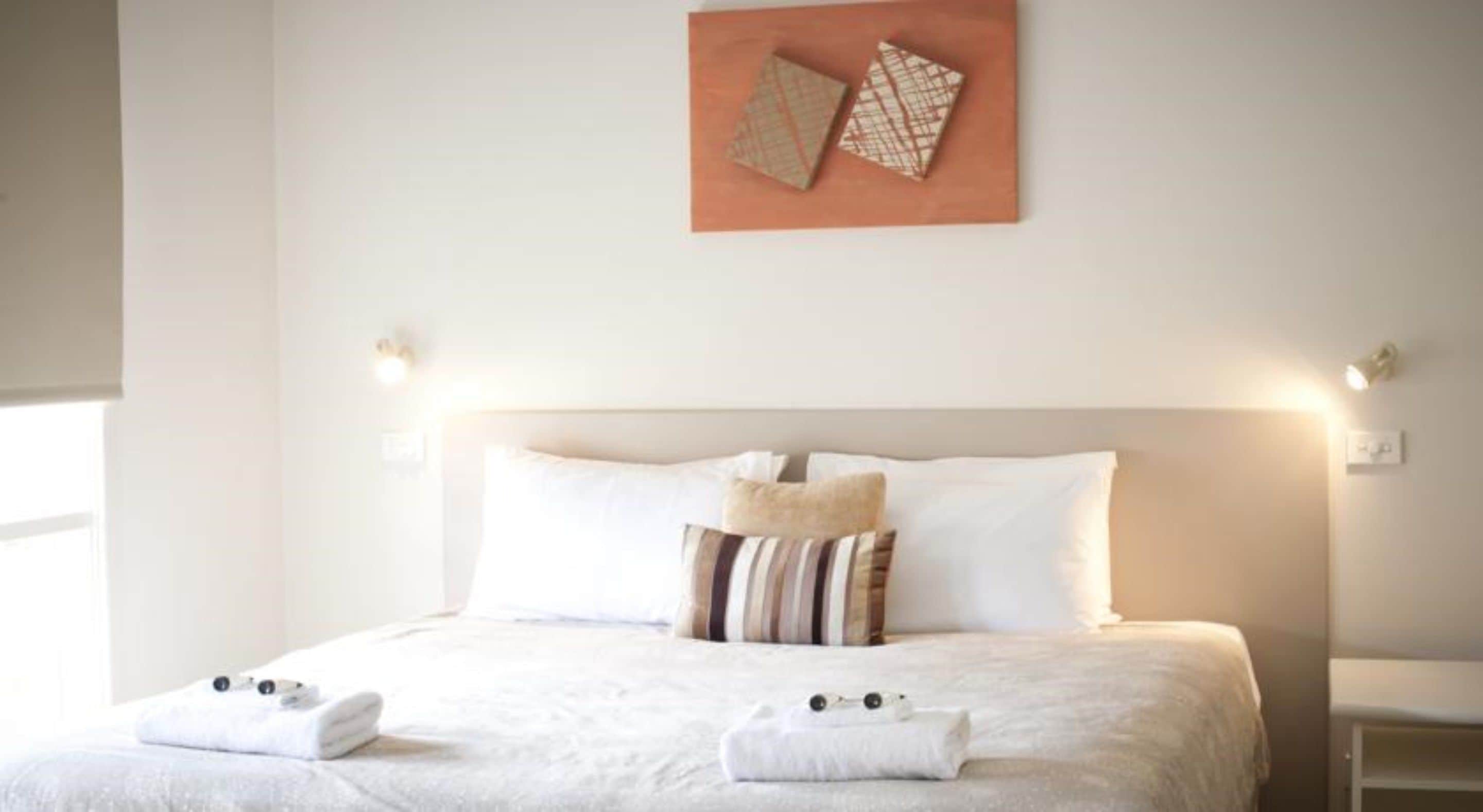 A neatly made bed with white linens, striped pillows, and two towels placed at the foot of the bed.