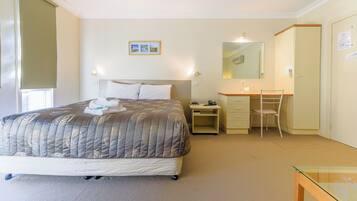 A hotel room with a bed, a desk with a chair, a mirror, and a small table.