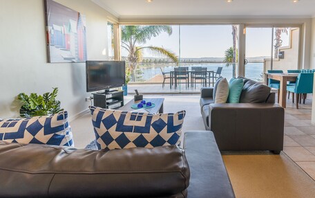 A modern living room with a sofa, a television, and a dining area with chairs and a table.