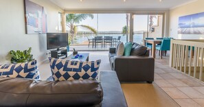 A modern living room with a sofa, a television, and a dining area with chairs and a table.