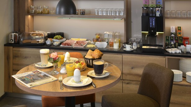 Una colazione servita su un tavolo di legno, con giornale, caffè e diversi prodotti per la colazione.