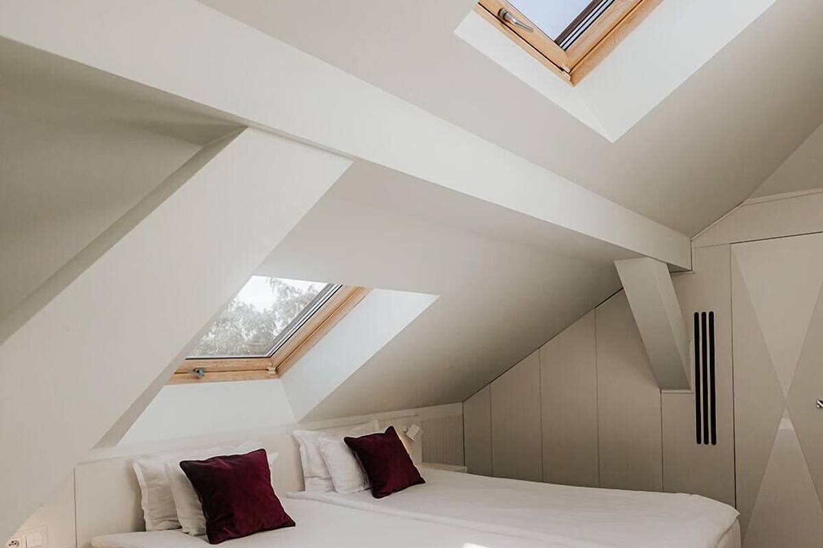 Ein modernes Schlafzimmer mit schrägen Wänden und Dachfenster, mit einem großen Bett, einem Nachttisch und integrierten Stauraum.