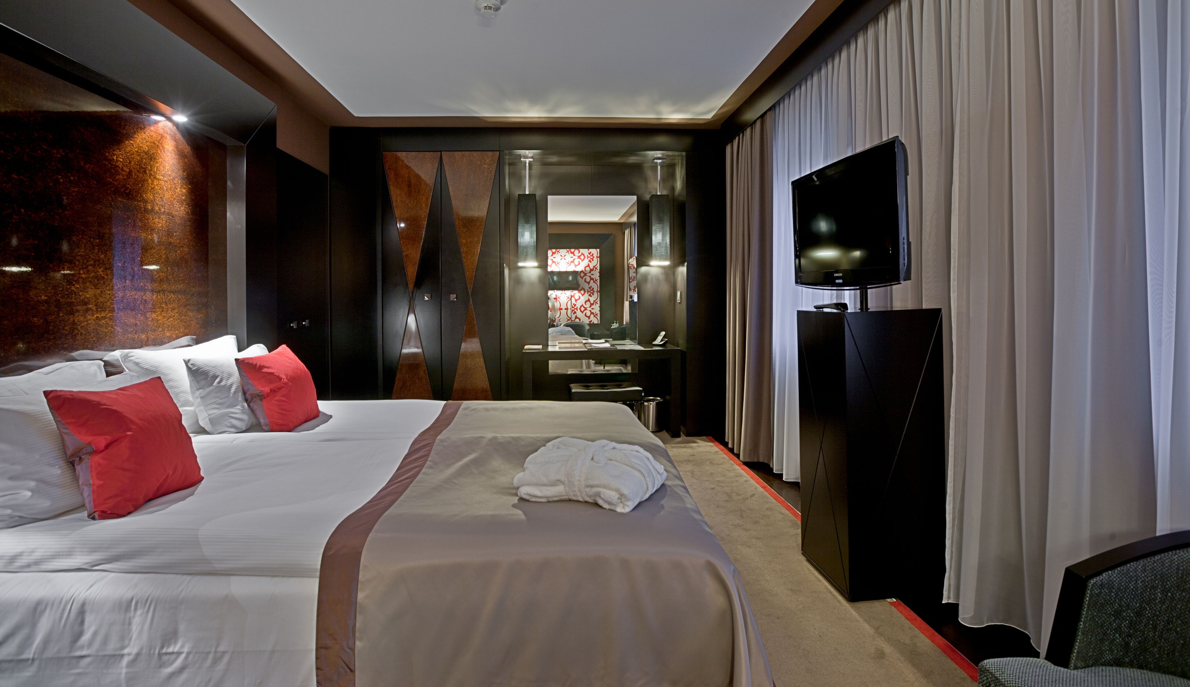 Ein Hotelzimmer mit einem großen Bett, einem Schreibtisch mit Flachbildfernseher und einem durchgegangenen Tür erkennbaren Badezimmer.