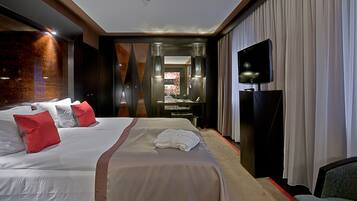 Ein Hotelzimmer mit einem großen Bett, einem Schreibtisch mit Flachbildfernseher und einem durchgegangenen Tür erkennbaren Badezimmer.