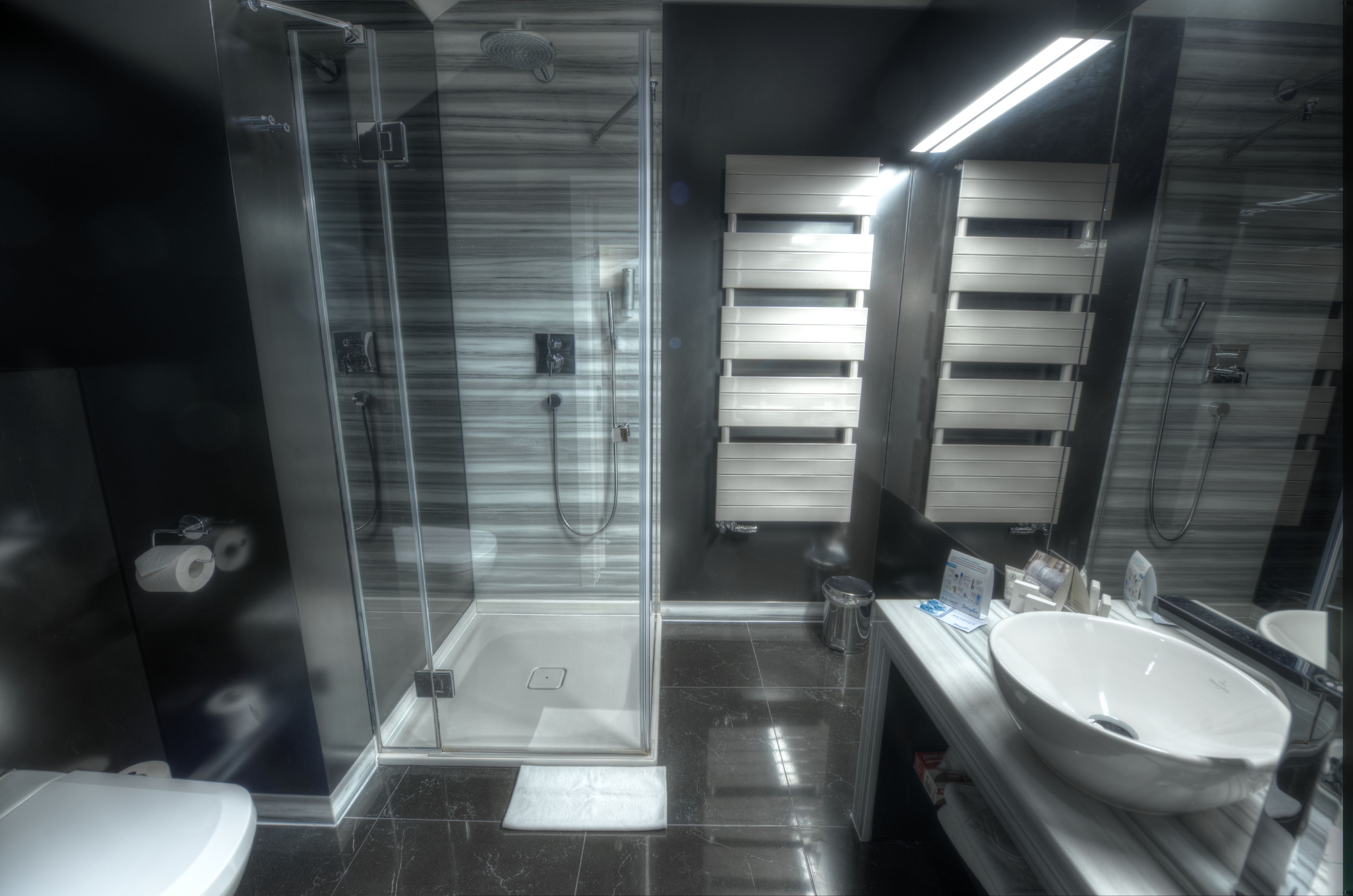 Un baño moderno con ducha de vidrio, lavamanos blanco y un espejo grande.