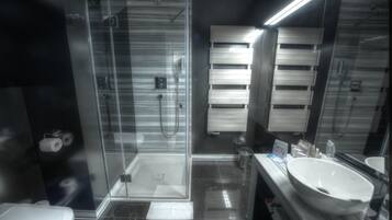 Un baño moderno con ducha de vidrio, lavamanos blanco y un espejo grande.