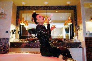 A woman sitting on a bathroom sink with a mirror above it, holding a glass of champagne.