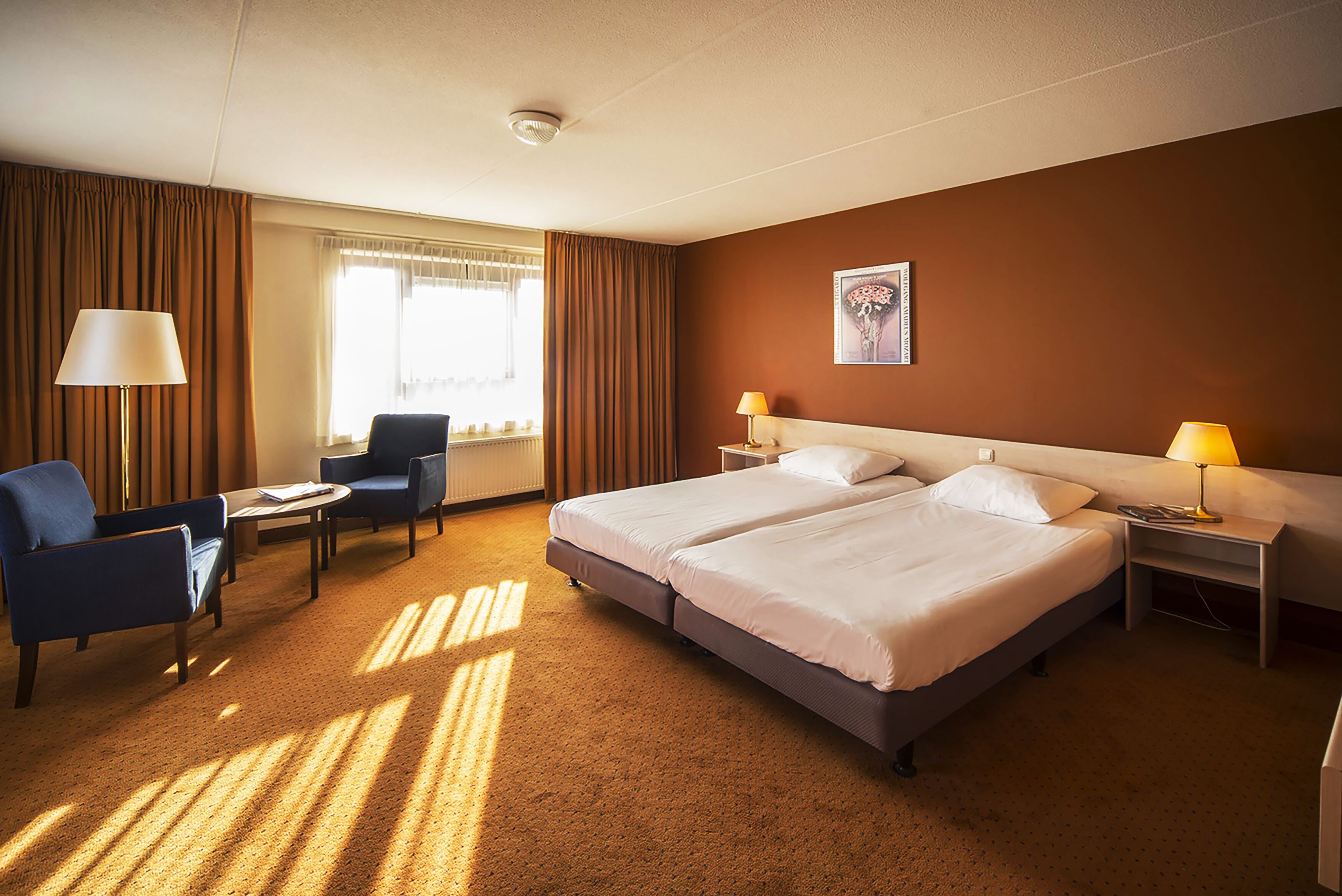 A hotel room with two beds, a desk, a chair, and a window with curtains.
