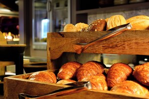 A wooden display case with various baked goods, including croissants and bread, in a bakery setting.