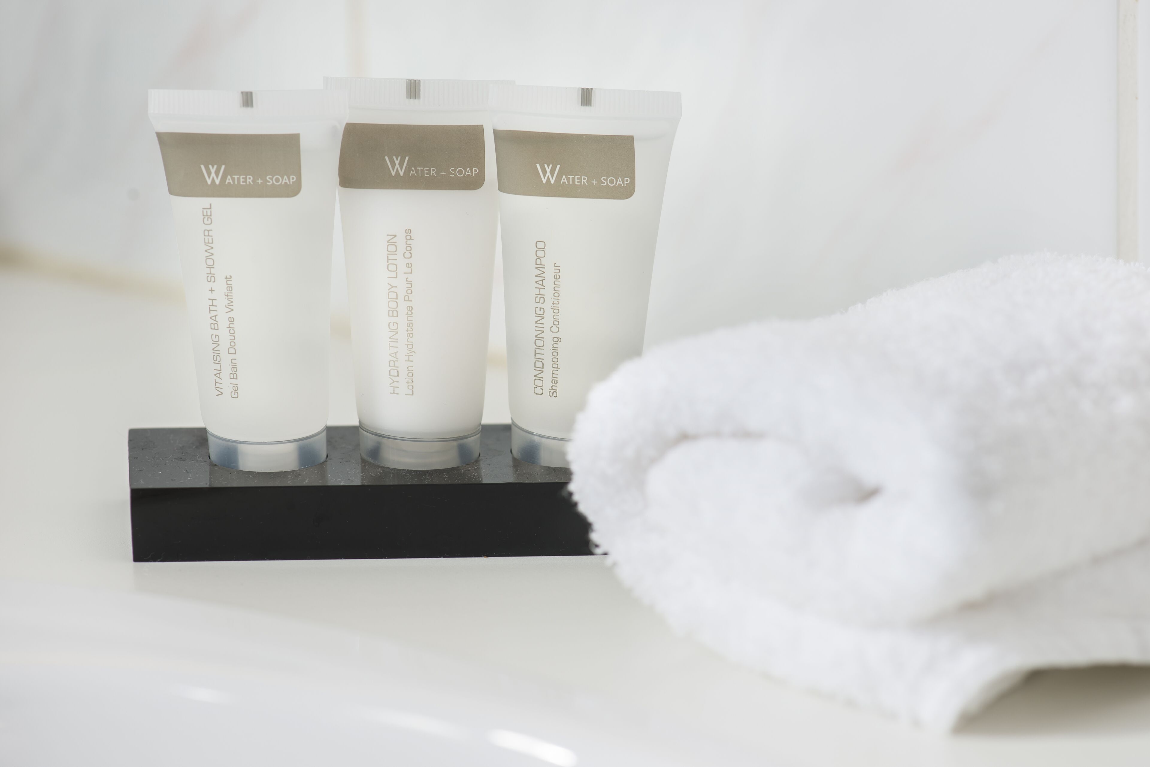 Three toiletry bottles on a black stand with a white towel beside them.