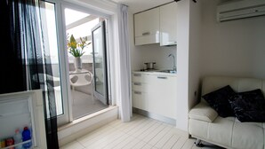 A compact living space with a kitchenette, a sofa, and a sliding glass door leading to an outdoor area. - Q Hotel (Rimini)
