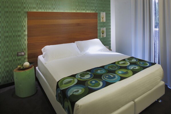 Una cama bien hecha con una colcha estampada, un cabecero de madera y una mesita de noche verde con un objeto decorativo.